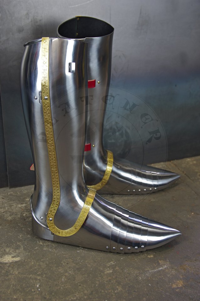 English style leg harness with fully closed cuisses, full greaves with characteristic line around outside ankles. Demi-greaves connected with greaves on rotary pin. Made of medium carbon steel of various thickness from 1 mm up to 1,5 mm. Heat hardened and tempered up to 42 HRC. Brass bands decoration motive based on example visible on Henry V tournament helm. Hand made steel buckles in set./Osony ng w stylu angielskim z w peni zamknitymi nabiodrkami, nagolennicami z charakterystyczn lini wok zewntrznej kostki. Demi-greave poczony z nagolennicami poprzez obrotowy pin. Wykonane ze stali redniowglowej rnej gruboci od 1 mm do 1,5 mm. Hartowane i odpuszczane do 42 HRC. Mosine listwy dekoracyjne z motywem wzorowanym na hemie turniejowym Henryka V. W zestawie rcznie robione sprzczki stalowe.